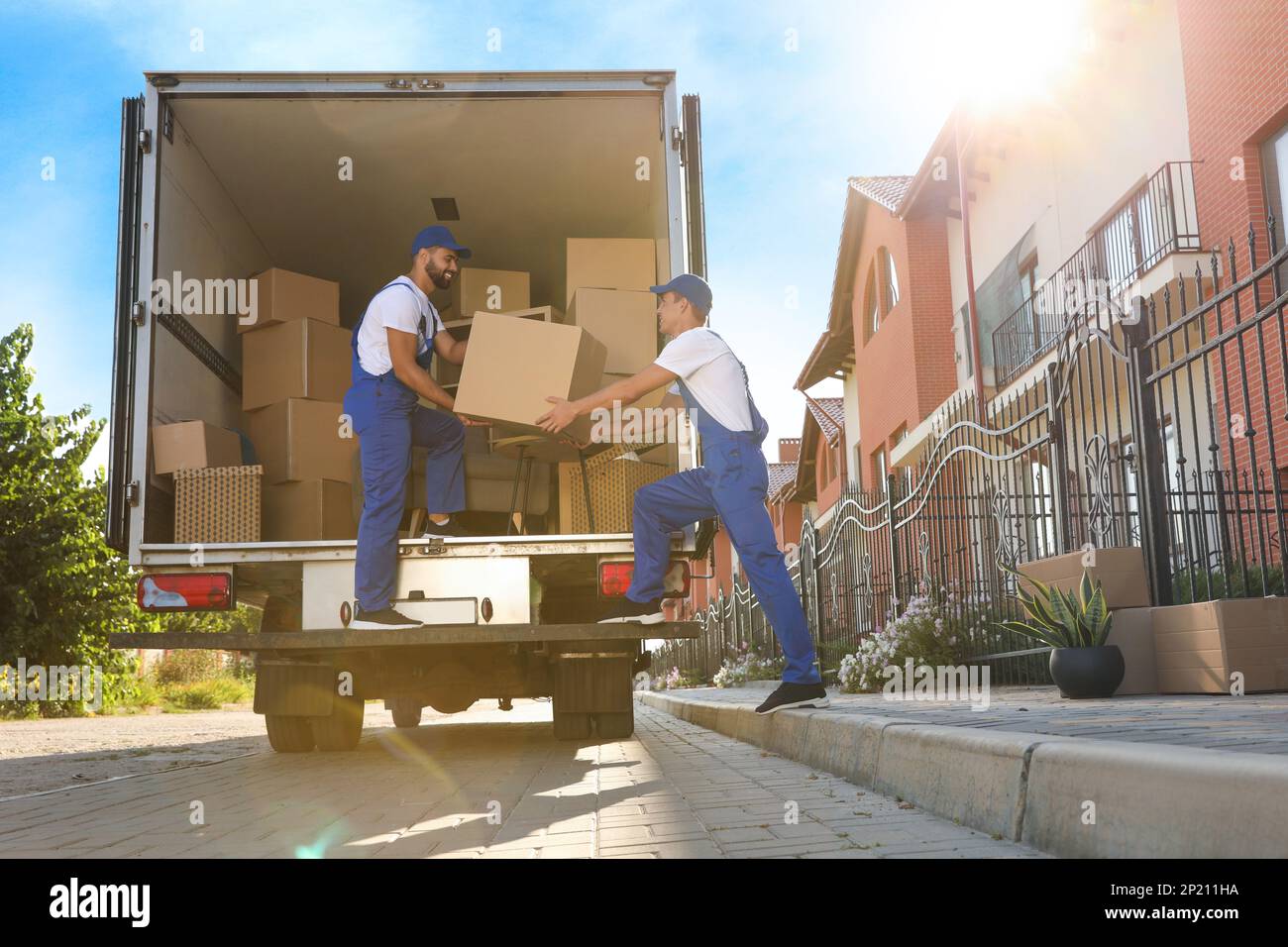 Arbeiter, die Kisten aus dem Lieferwagen im Freien entladen. Umzugsdienst Stockfoto