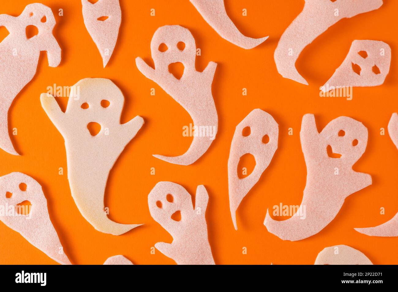 Weiße Geister basteln Kinder für Halloween. Geschenkpapier-Ghost auf orangefarbenem Hintergrund, Draufsicht. Ein unheimliches und lustiges Monsterspielzeug mit eigenen Händen. Cartoon gruseliges Flüstern. Handgemacht. Legt Boo-Zeichen fest Stockfoto