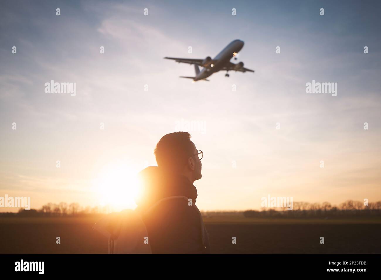 Mann mit Rucksack, der auf die Flugzeuglandung am Flughafen während des wunderschönen Sonnenuntergangs blickt. Stockfoto