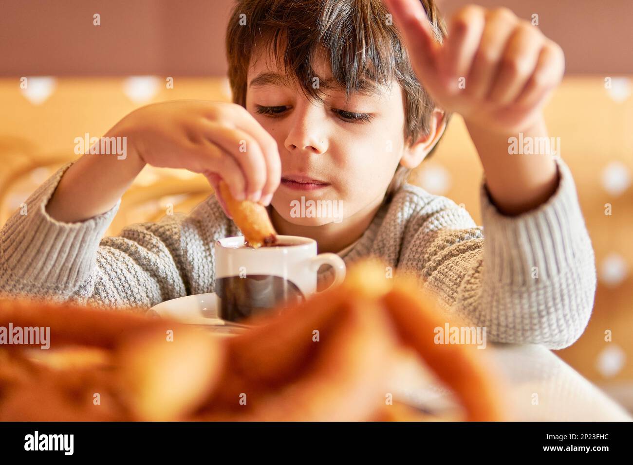 Ein Kind im Grundalter, das Churros in eine heiße Schokoladentasse taucht Stockfoto