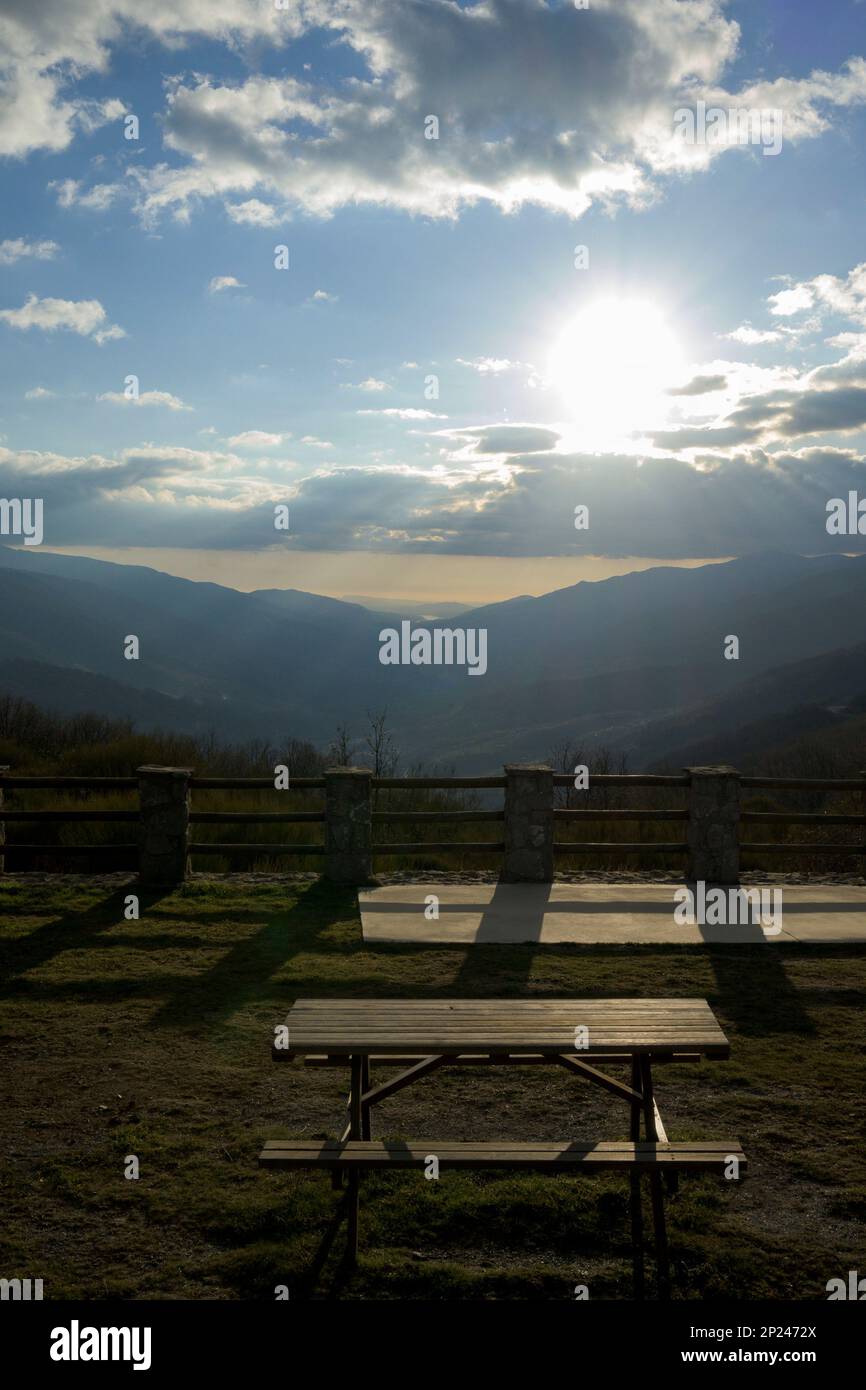 Picknicktisch mit Blick auf das Jerte-Tal bei Sonnenuntergang im Winter, vertikal mit Sonne zwischen den Wolken Stockfoto