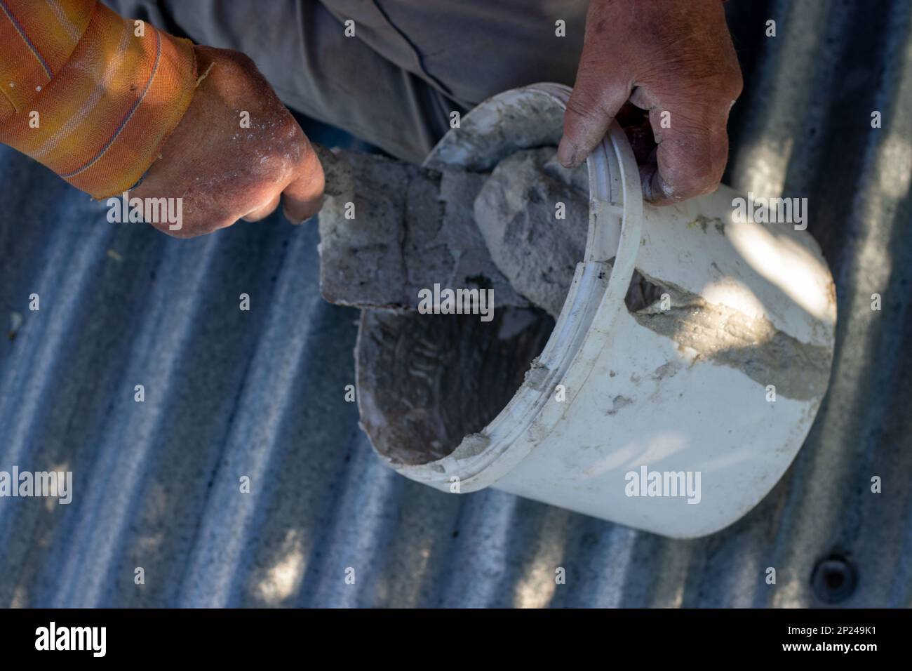 Ein Mann sitzt auf dem Dach und füllt den Eimer mit Zementmörtel. Selektiver Fokus Stockfoto