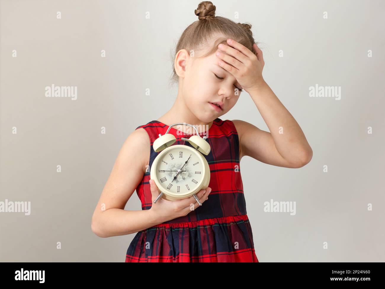 Niedliches Kind mit geschlossenen Augen und Hand am Kopf mit Weckfunktion Konzept, um früh aufzuwachen, weißliches kleines Mädchen im Alter von 6 7 Jahren in rotem Karomuster Stockfoto