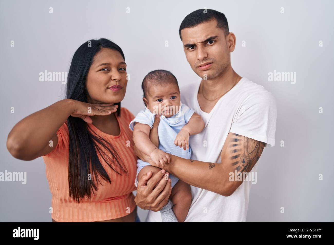 Ein junges lateinamerikanisches Paar mit einem Baby, das über einem isolierten Hintergrund steht und mit der Hand als Messer die Kehle durchschneidet, droht Aggression mit wütender Geige Stockfoto