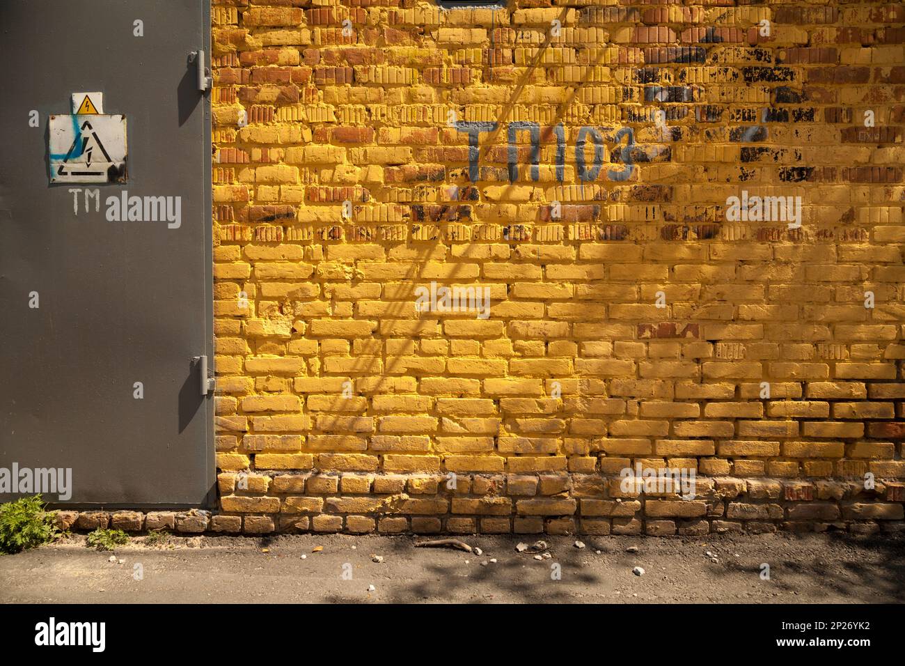 Lebhafte gelbe Ziegel Wand Hintergrund mit einer Tür und ein Gefahrenzeichen Hochspannung. Schmutzige Grunge Industriekulisse mit Zeichen, Buchstaben und Zahlen Stockfoto