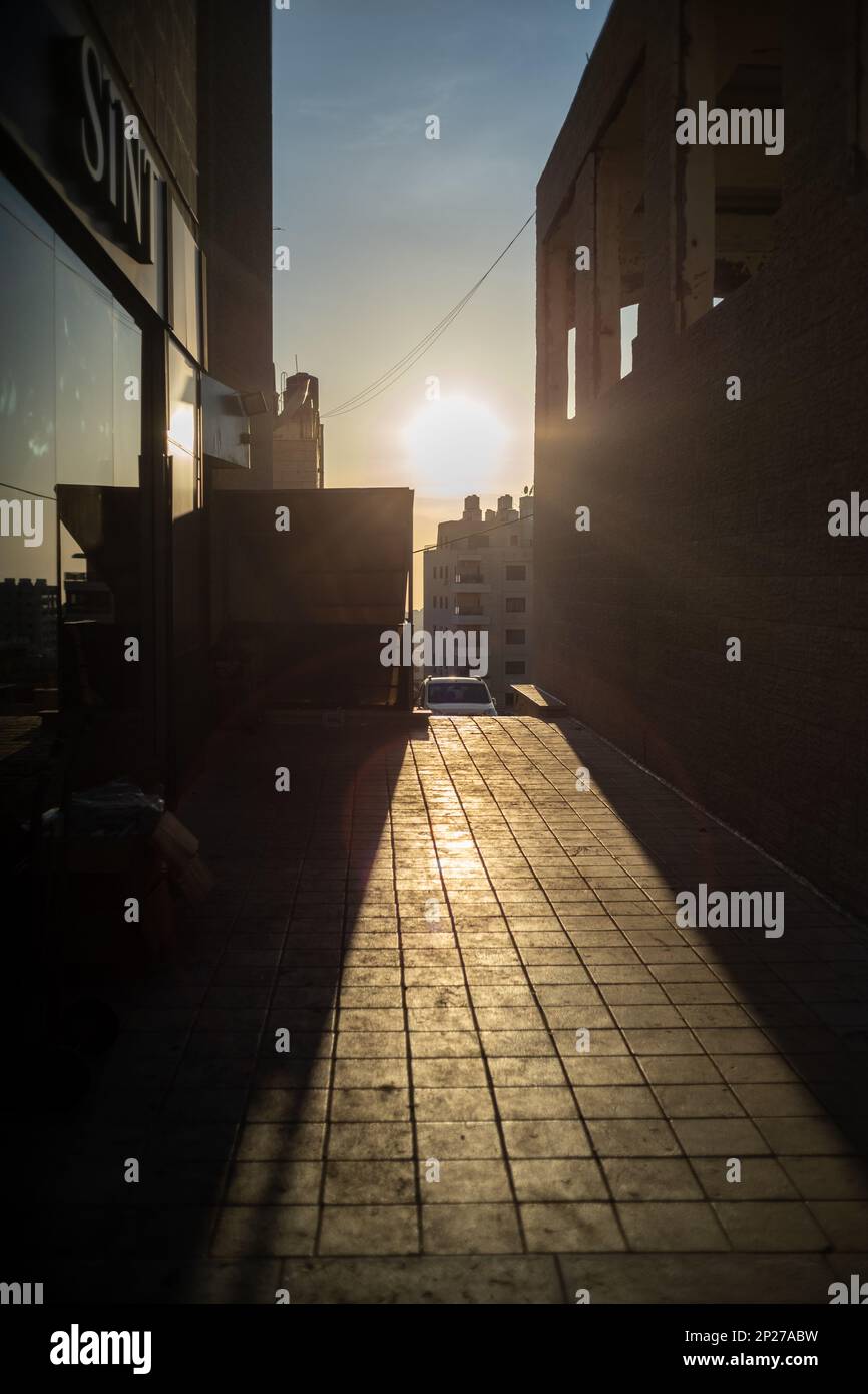 Schmale Fliesen leerer Durchgang zwischen hohen Wänden mit Blick auf die Sonne bei Sonnenuntergang Stockfoto