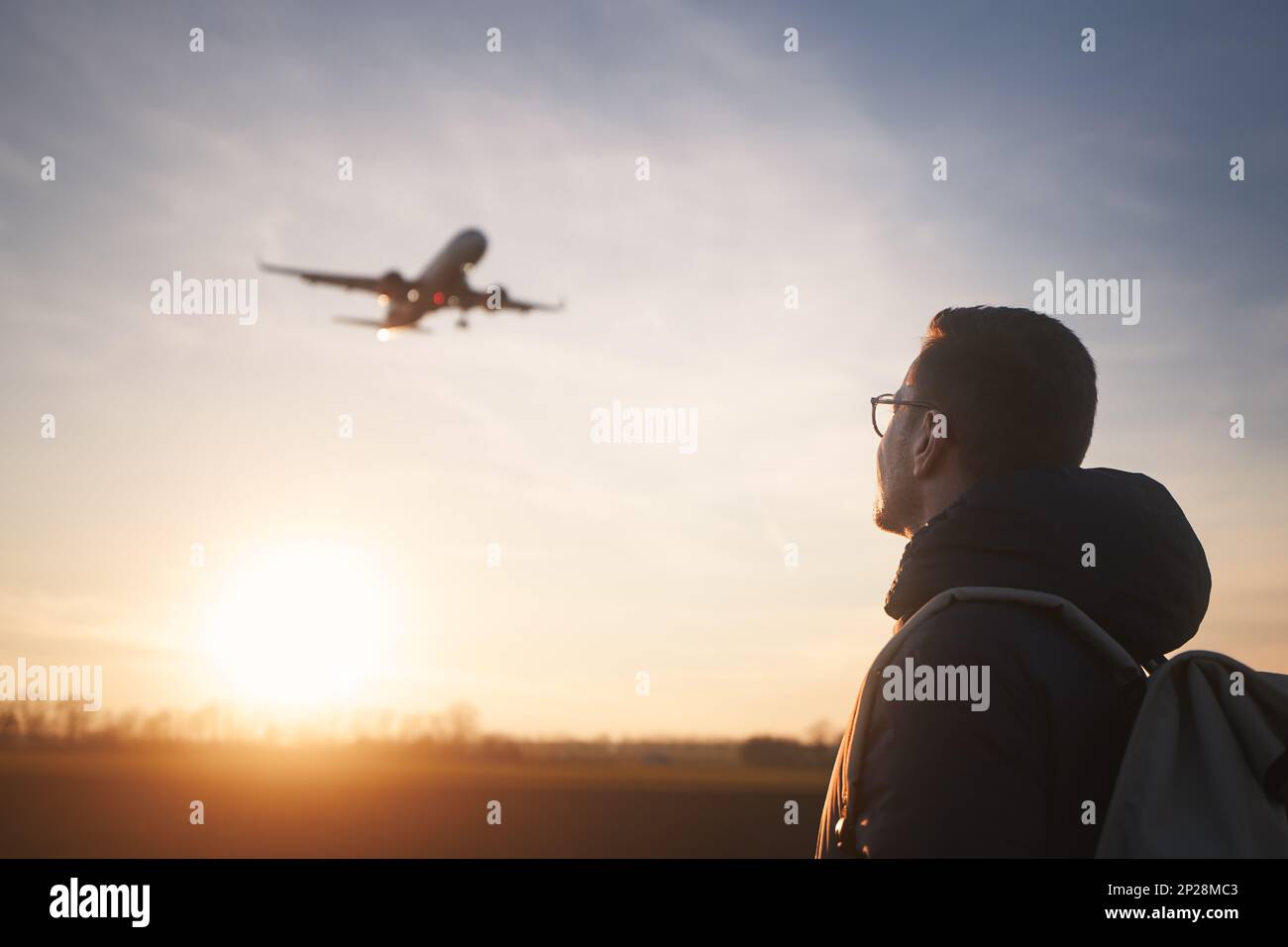 Mann mit Rucksack, der auf die Flugzeuglandung am Flughafen während des wunderschönen Sonnenuntergangs blickt. Stockfoto