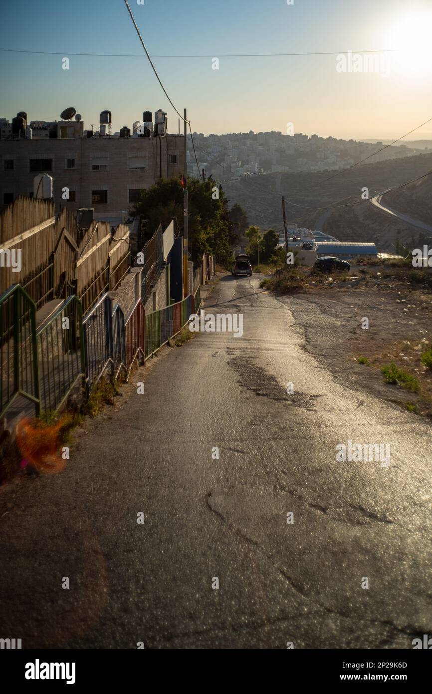Steile, leere Straße mit zwei schwarzen Autos geparkt, Dschunks auf einem Grundstück, mit einem Lens Flare, Foggy Air mit Blick auf die strahlende Sonne Stockfoto