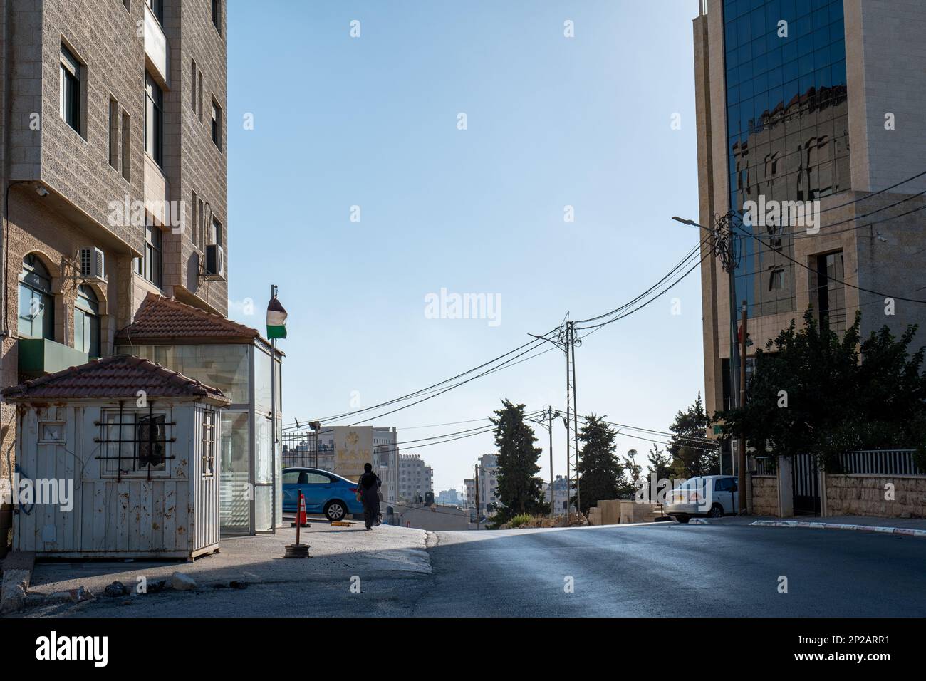 Ramallah, Ramallah und al-Bireh Governorate, Palästina - 24. Juli 2022: Woman in Black Walk in an empty Avenue at Dawn mit Hochhäusern, Bäumen und Stockfoto