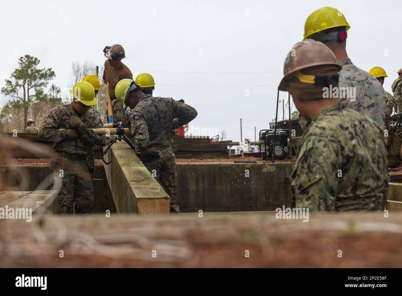 USA Marines mit 8. Engineer Support Batailion, Combat Logistics Regiment 27, 2. Marine Logistics Group und USA Navy Sailers mit Naval Mobile Construction Battalion 133 manövrieren einen Holzbalken, um eine Holzbrücke während des Trainings Winter Pioneer 23 in Camp Lejeune, North Carolina, am 31. Januar 2023 zu bauen. Winter Pioneer 23 ist eine Übung auf taktischer Ebene, die integrierte US-amerikanische Marine Corps Engineer und US Bautrupps der Marine, um einen fortgeschrittenen Marinestützpunkt zu errichten und zu erhalten, fortgeschrittene Expeditionsstützpunkte zu errichten und zur Sensibilisierung für den maritimen Bereich beizutragen. Stockfoto