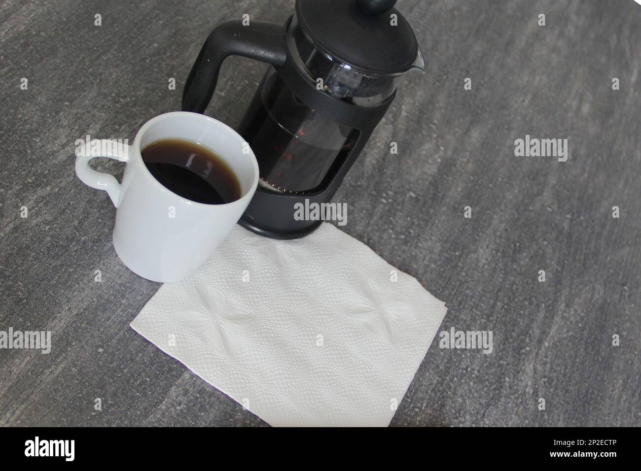 Eine Tasse Kaffee, eine französische Presse und eine weiße Serviette für eine Nachricht Stockfoto