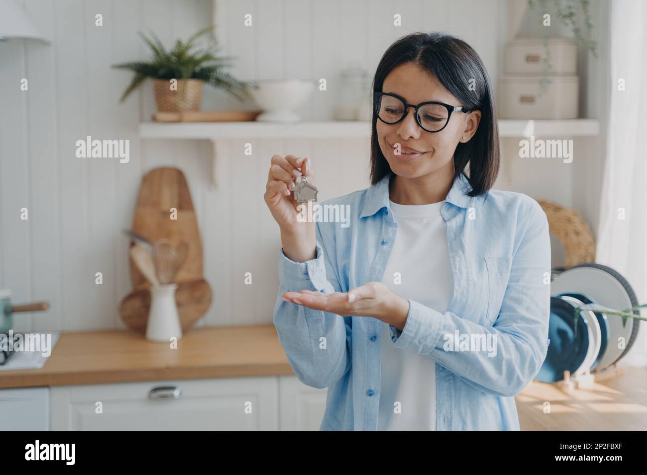 Glückliche Hausbesitzerin oder Mieterin, die Schlüssel zum neuen Zuhause zeigt, steht in der Küche. Frau mit Schlüssel für Haus oder Wohnung, zufrieden mit dem Wohnungsbau Stockfoto