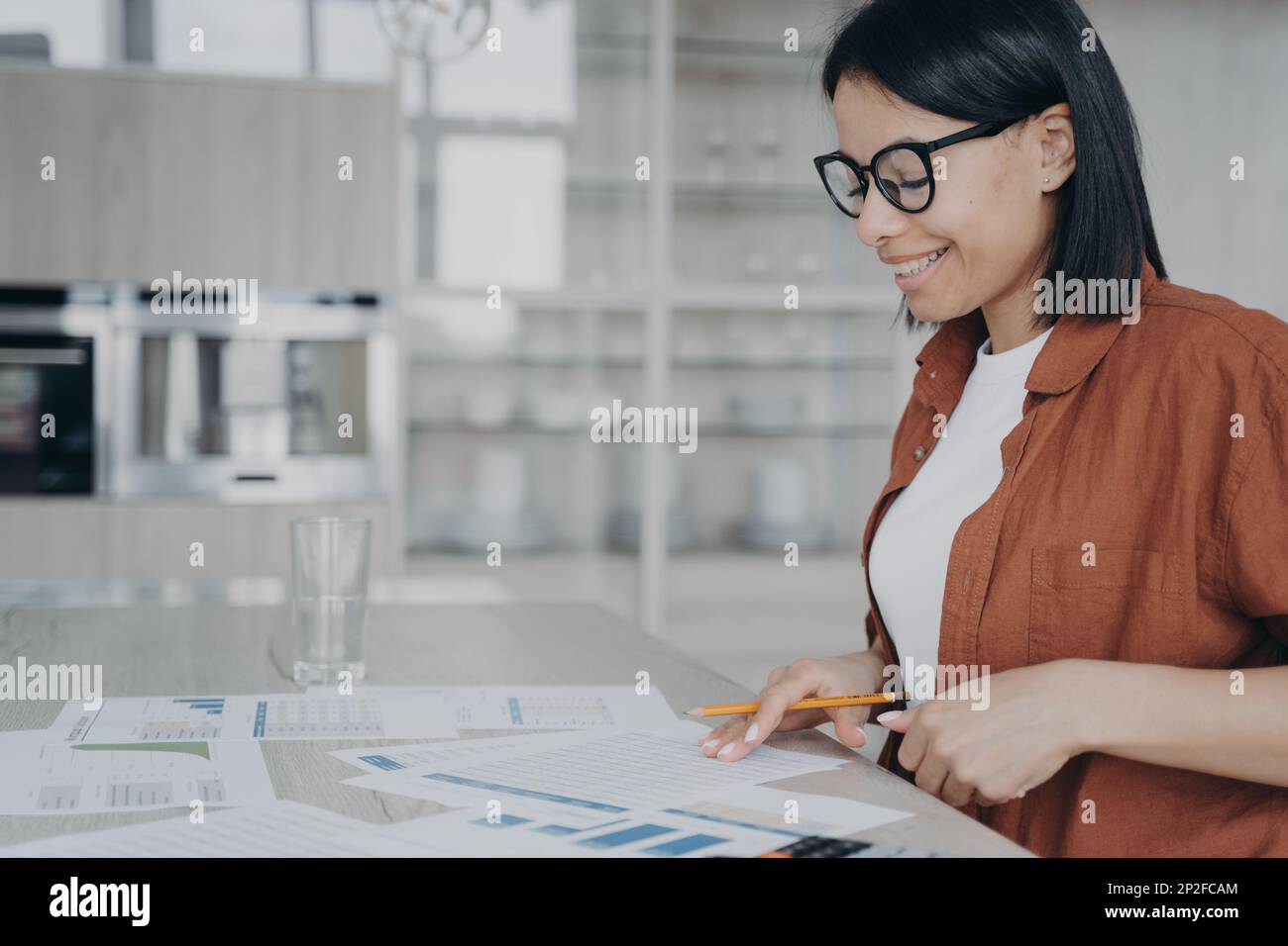 Lächelnde Geschäftsfrau mit Brille, die statistische Daten analysiert, die an Finanzprojekten oder Startup-Präsentationen arbeiten. Eine nette Angestellte, die das Dokum überprüft Stockfoto