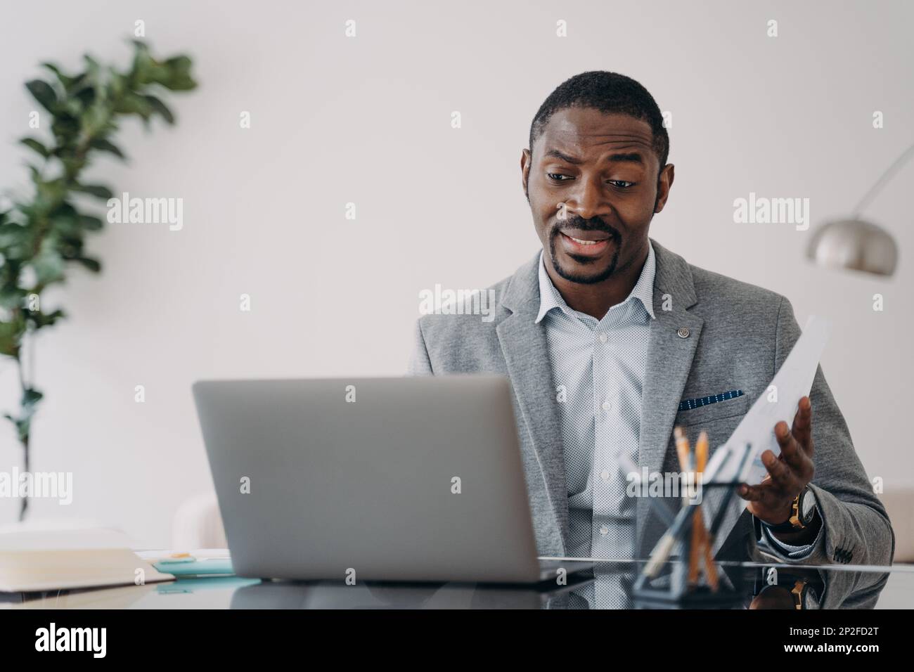 Ein verblüffter afroamerikanischer Arbeiter, der sich den Laptop-Bildschirm anschaute, erhielt eine Kündigungsmitteilung. Verwirrter schwarzer Geschäftsmann, der schlechte Nachrichten in E-Mails liest Stockfoto