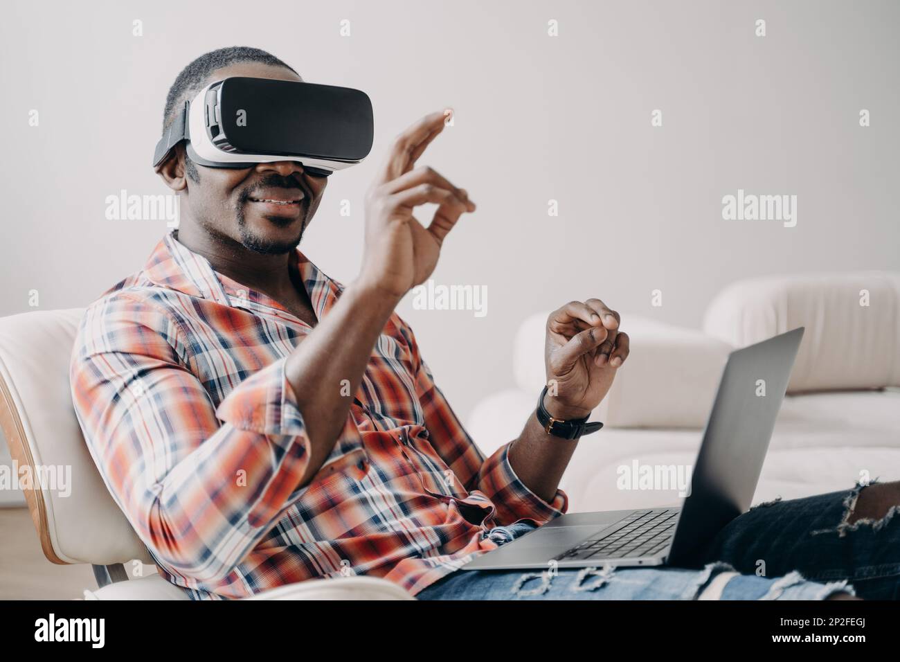 Ferne Arbeit und futuristisches Gaming. afroamerikaner mit Brille, die zu Hause mit einem Laptop arbeitet. Entspannter Freiberufler klickt auf virtuelle Schaltflächen. Intern Stockfoto
