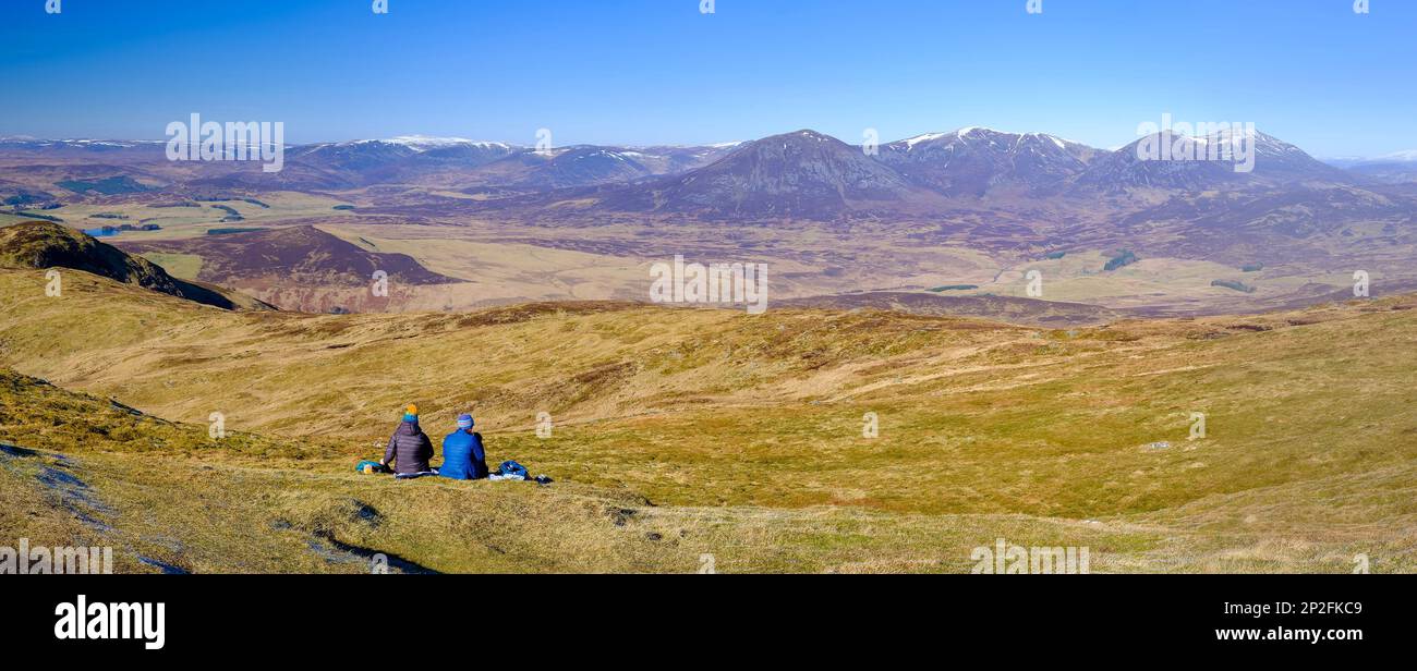 Zwei Wanderinnen, die sich auf dem Gipfel von Ben Vorlich in der Nähe von Pitlochry, Schottland, entspannen und die weitläufige Aussicht genießen Stockfoto