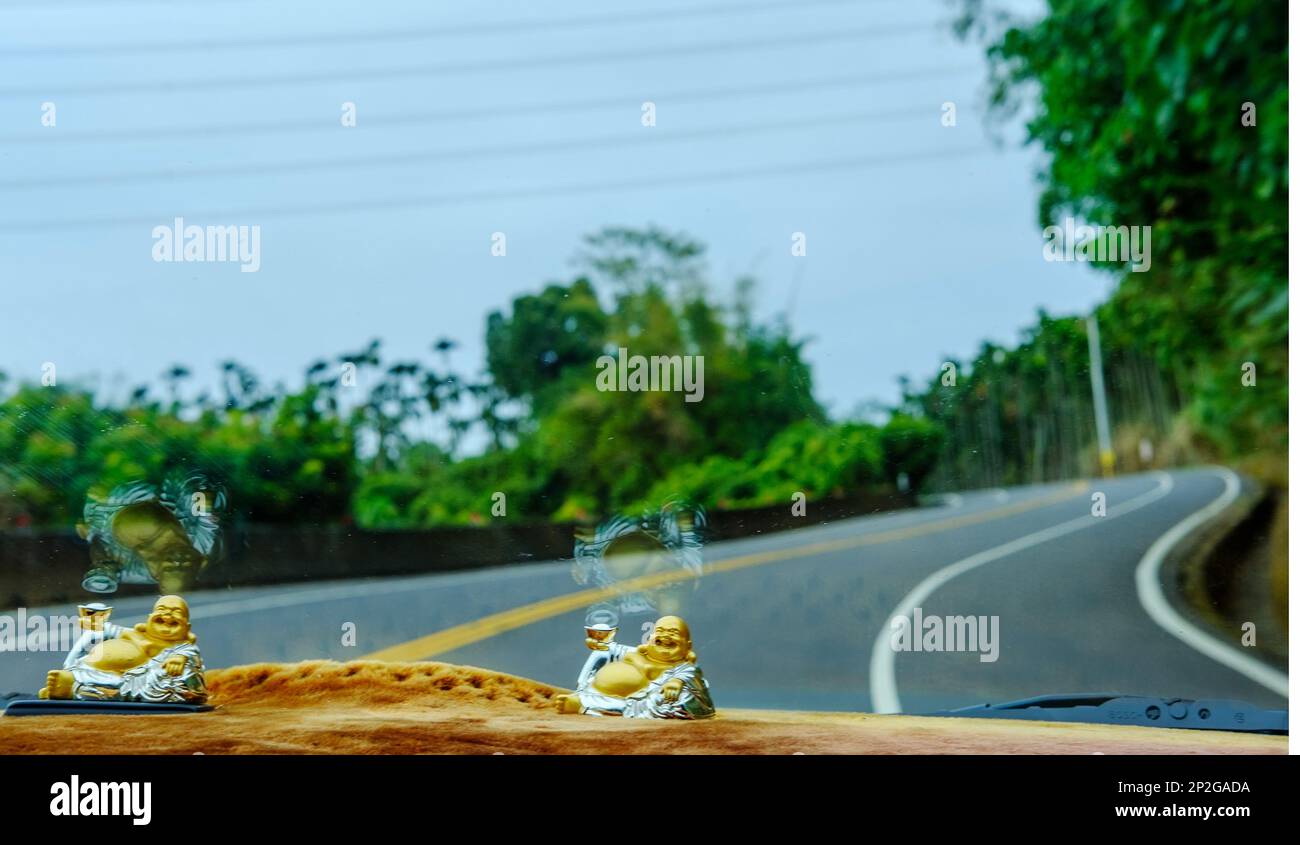 Ein Blick auf eine offene Straße durch die Windschutzscheibe von einem Auto aus mit Buddha-Statuen auf dem Armaturenbrett Stockfoto