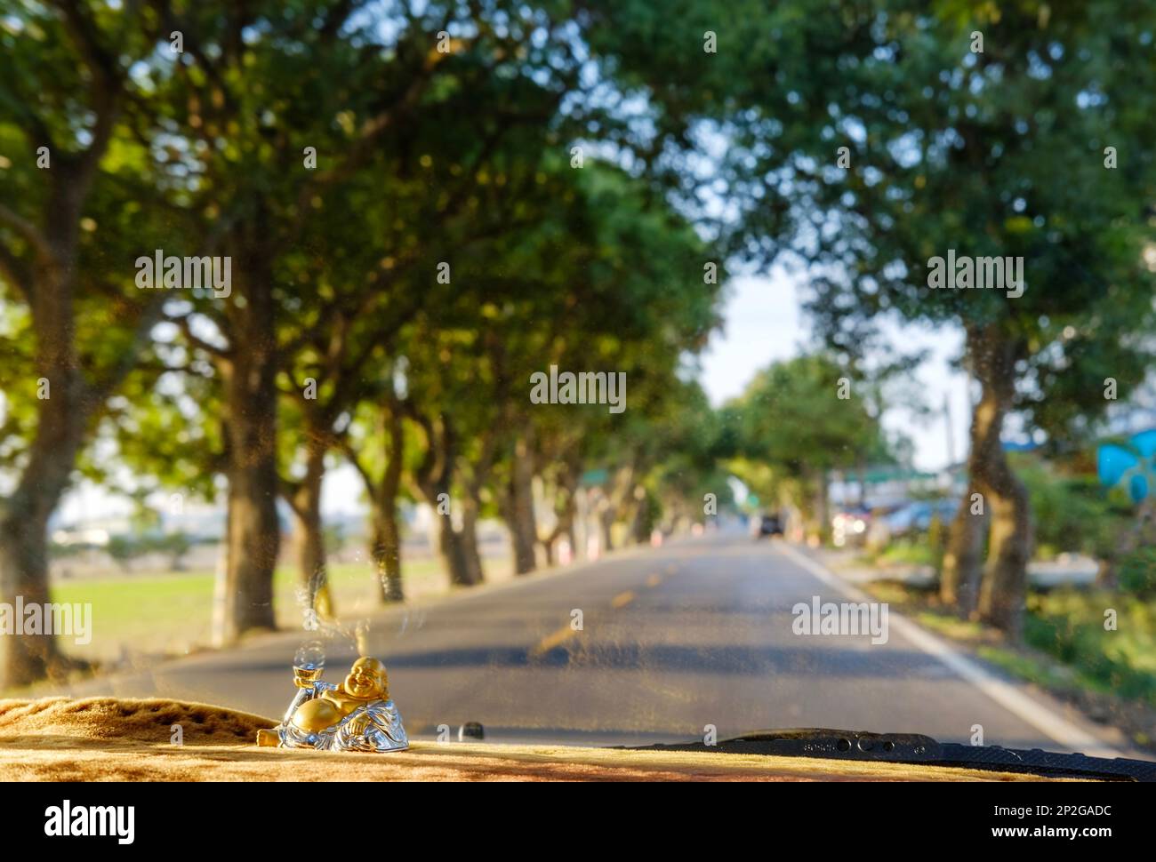 Ein Blick auf eine offene Straße durch die Windschutzscheibe von einem Auto aus mit Buddha-Statuen auf dem Armaturenbrett Stockfoto