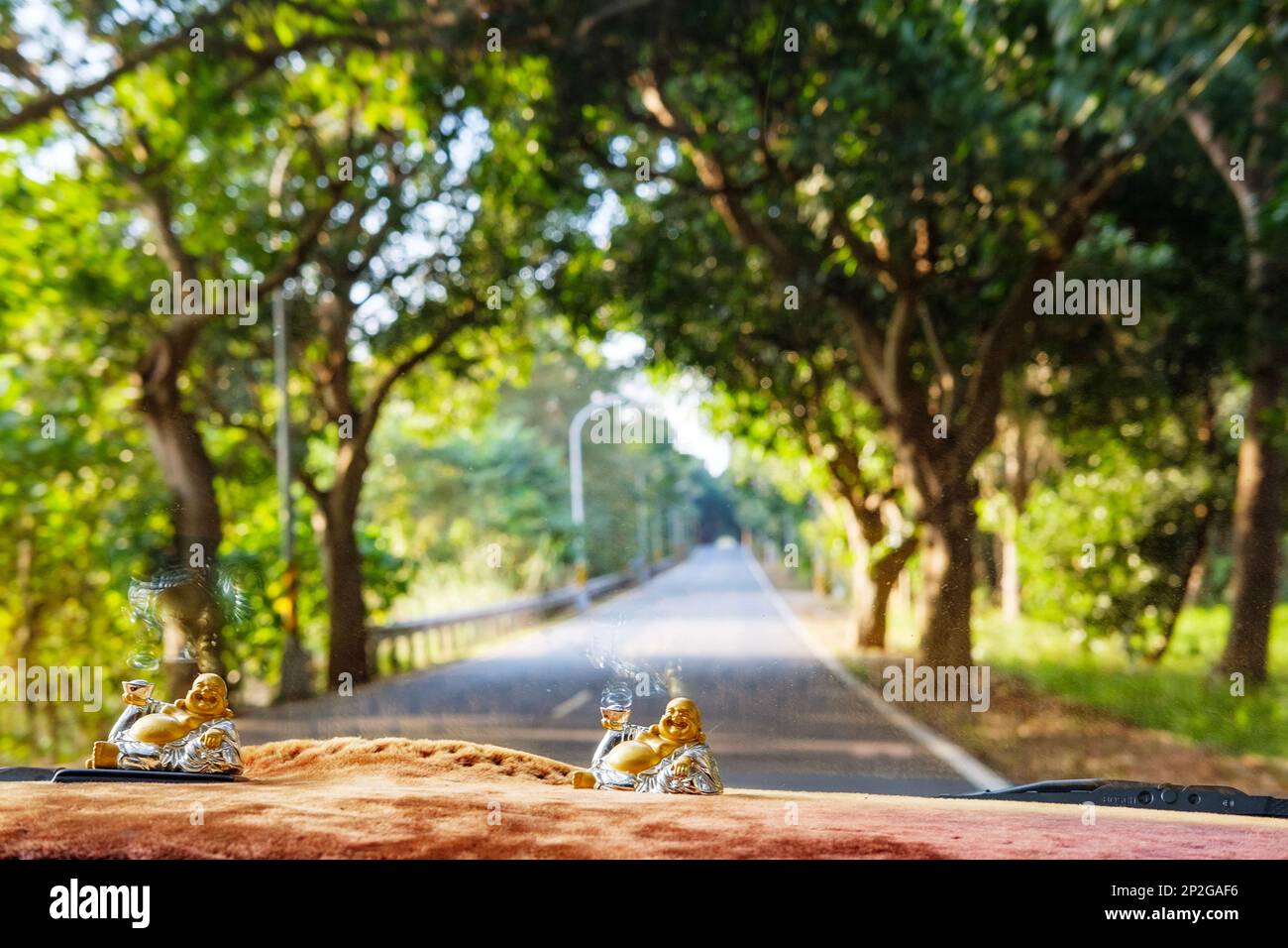 Ein Blick auf eine offene Straße durch die Windschutzscheibe von einem Auto aus mit Buddha-Statuen auf dem Armaturenbrett Stockfoto