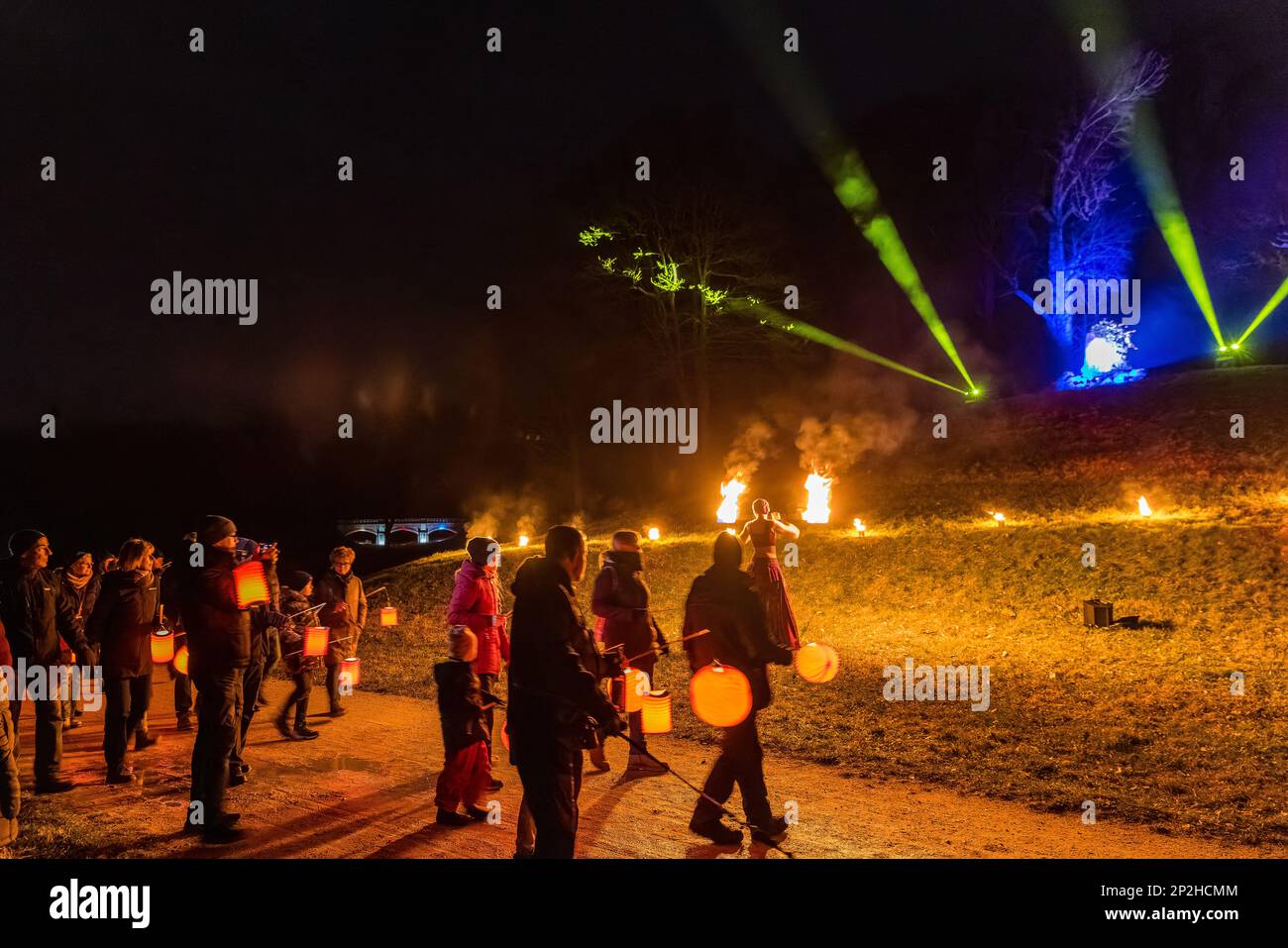 Leknica, Polen. 04. März 2023. Besucher stehen auf der polnischen Seite des Pückler Parks, wo eine Feuertänzerin eine Show veranstaltet. Auf dem Winter Light Festival, nach zwei Jahren Pause, Mehr als 1.000 Besucher wanderten von fünf verschiedenen Orten im Park, von Bad Muskau in Deutschland und ··knica in Polen im Licht ihrer Laternen, vorbei an bunt beleuchteten Gebäuden und Baumgruppen zur festlich beleuchteten Neuen Burg. Auf dem Burggarten konnten sich die Wanderer stärken und Live-Swing-Musik hören und anschauen. Kredit: Frank Hammerschmidt/dpa/Alamy Live News Stockfoto