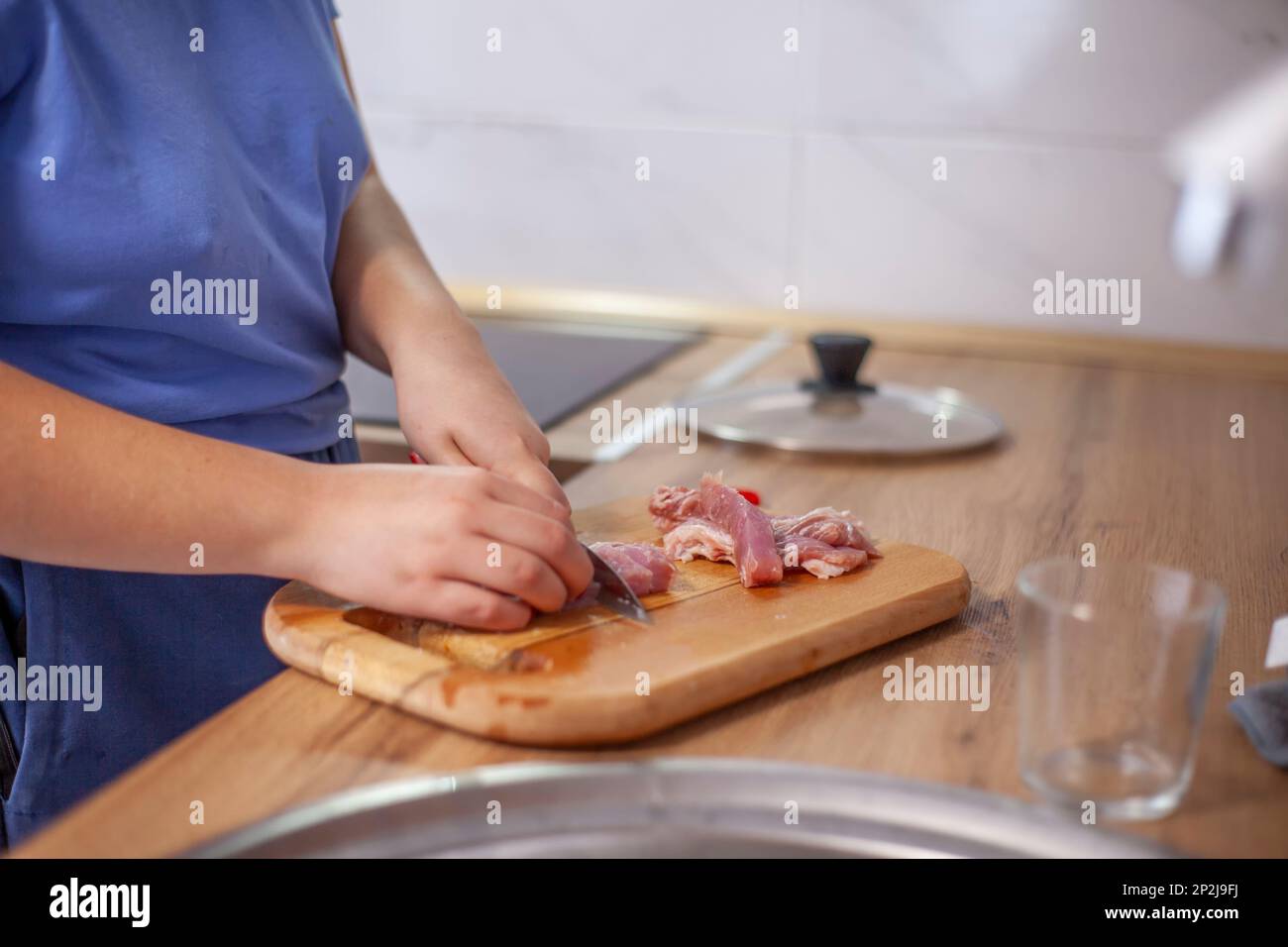 Fleisch auf einem Brett schneiden, Frauenhände mit einem Messer. Unverstellter natürlicher Schuss einer Frau beim Kochen in der Küche Stockfoto