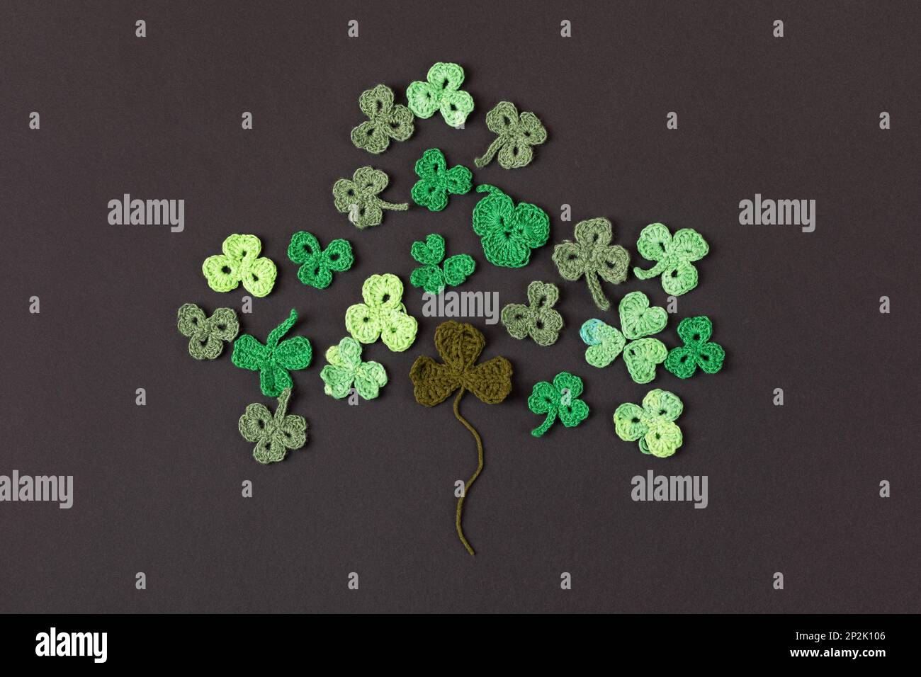 St. Patrick's Day Konzept. Komposition aus gestrickten grünen Shamrocks in Form von dreiblättrigem Klee auf schwarzem Hintergrund. Weihnachtsschild und Strick Stockfoto