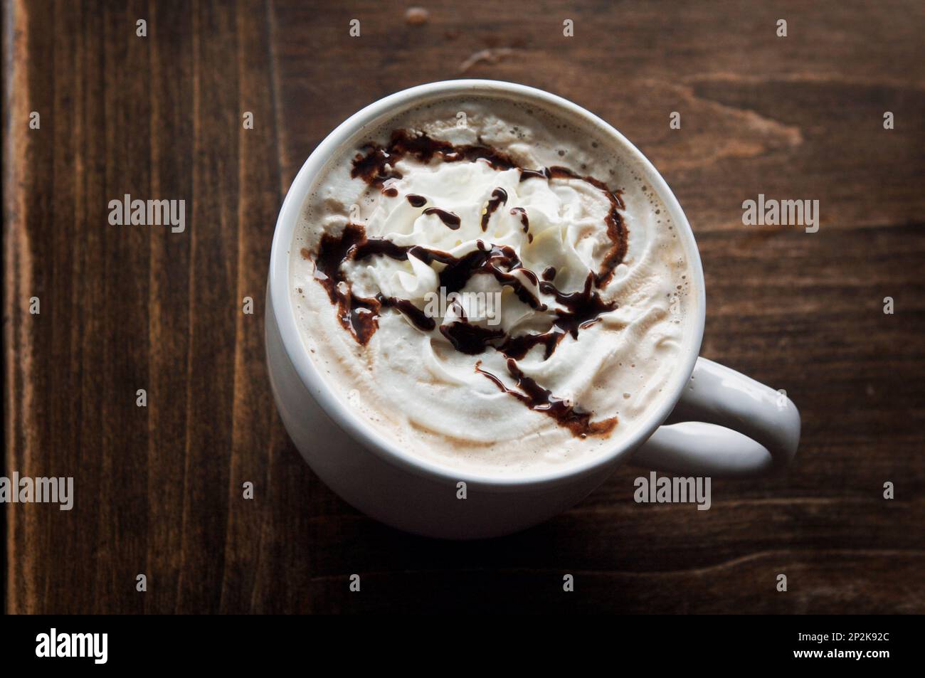 Blick hinunter auf eine Tasse heißen Mokkakaffee mit Schlagsahne und getrunkener Schokolade auf einem dunkelbraunen Holztisch. Stockfoto