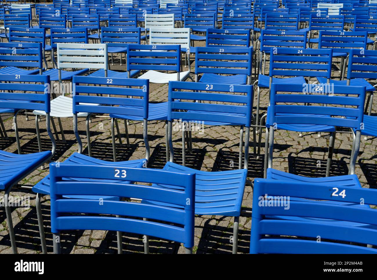 Leere blau-weiße Stühle mit Nummern auf einem kopfsteingepflasterten Platz, vorbereitet für eine Open-Air-Veranstaltung Stockfoto