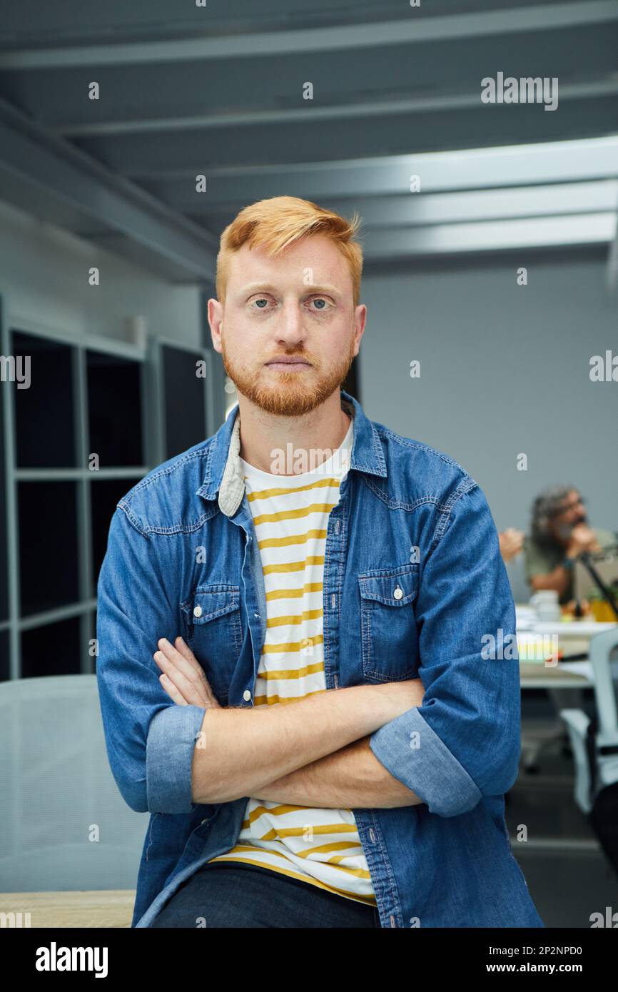 Ein junger, rothaariger Programmierer oder Geschäftsmann in einem modernen Büro, der ernsthaft in die Kamera schaut. Stockfoto