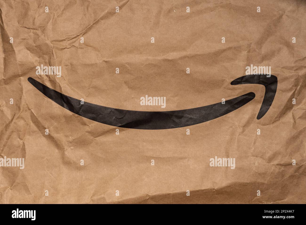 Geschwungener Amazon-Pfeil auf einer Verpackung. Schwarzer Lächelpfeil auf braunem Papier. Berühmtes E-Commerce-Logo auf zerknittertem Hintergrund. Stockfoto