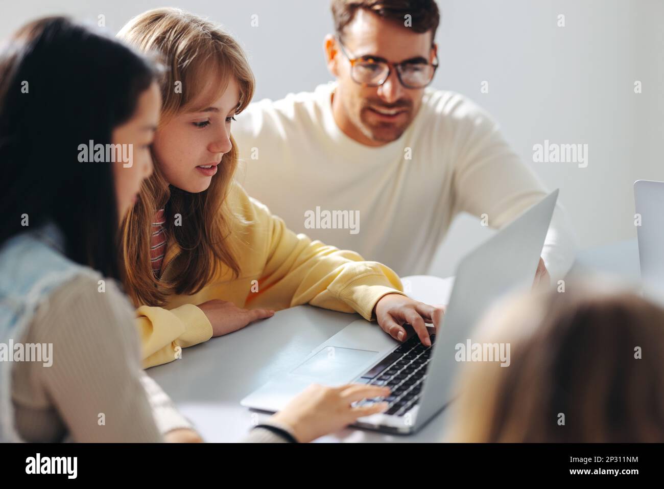 Junge Mädchen, die an einem Computerkurs teilnehmen, mit einem Lehrer, der sie in einer Programmierstunde führt. Männlicher Erzieher, der digitale Bildung und eine starke Entdeckung anbietet Stockfoto