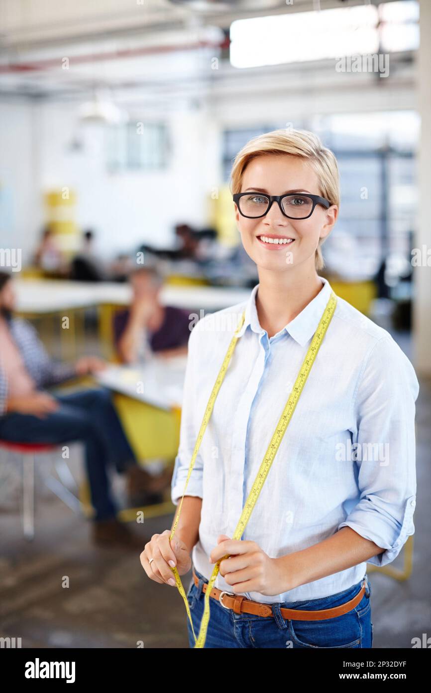 Der Maßstab für den Erfolg. Porträt einer jungen Frau mit einem Maßband um den Hals und Kollegen im Hintergrund. Stockfoto