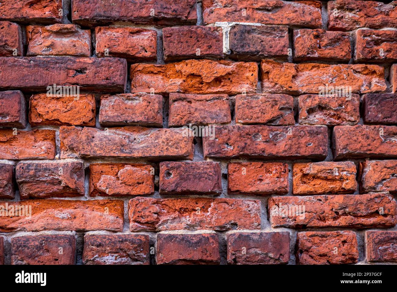Die Nahaufnahme einer verwitterten Backsteinwand zeigt ein Zusammenspiel verschiedener Rottöne, von rostigem Orange bis violett. Stockfoto