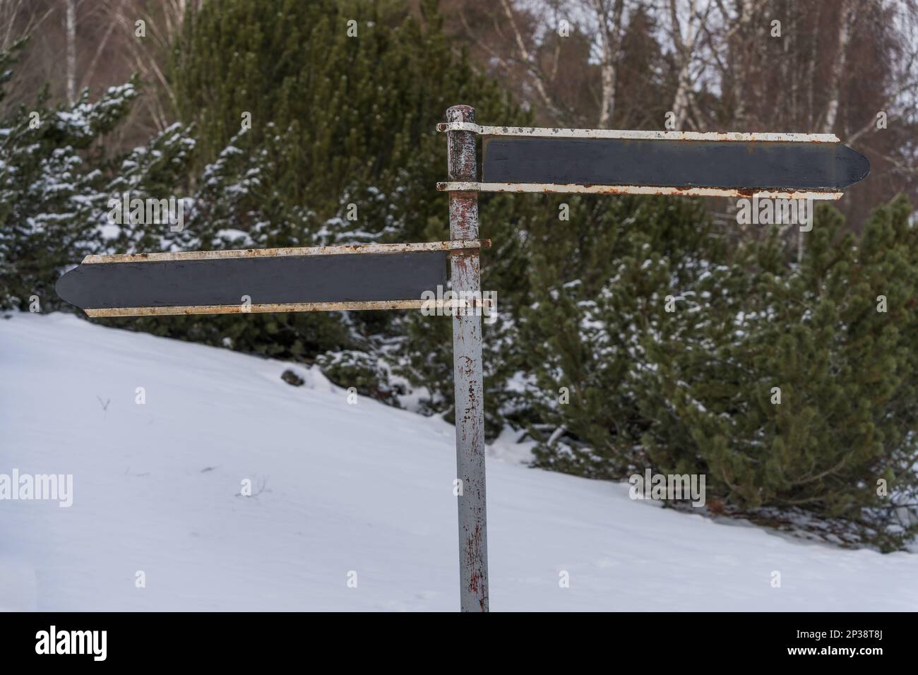 Rostiges, rostiges Hinweisschild im Winter, das in zwei Richtungen zeigt. Stockfoto