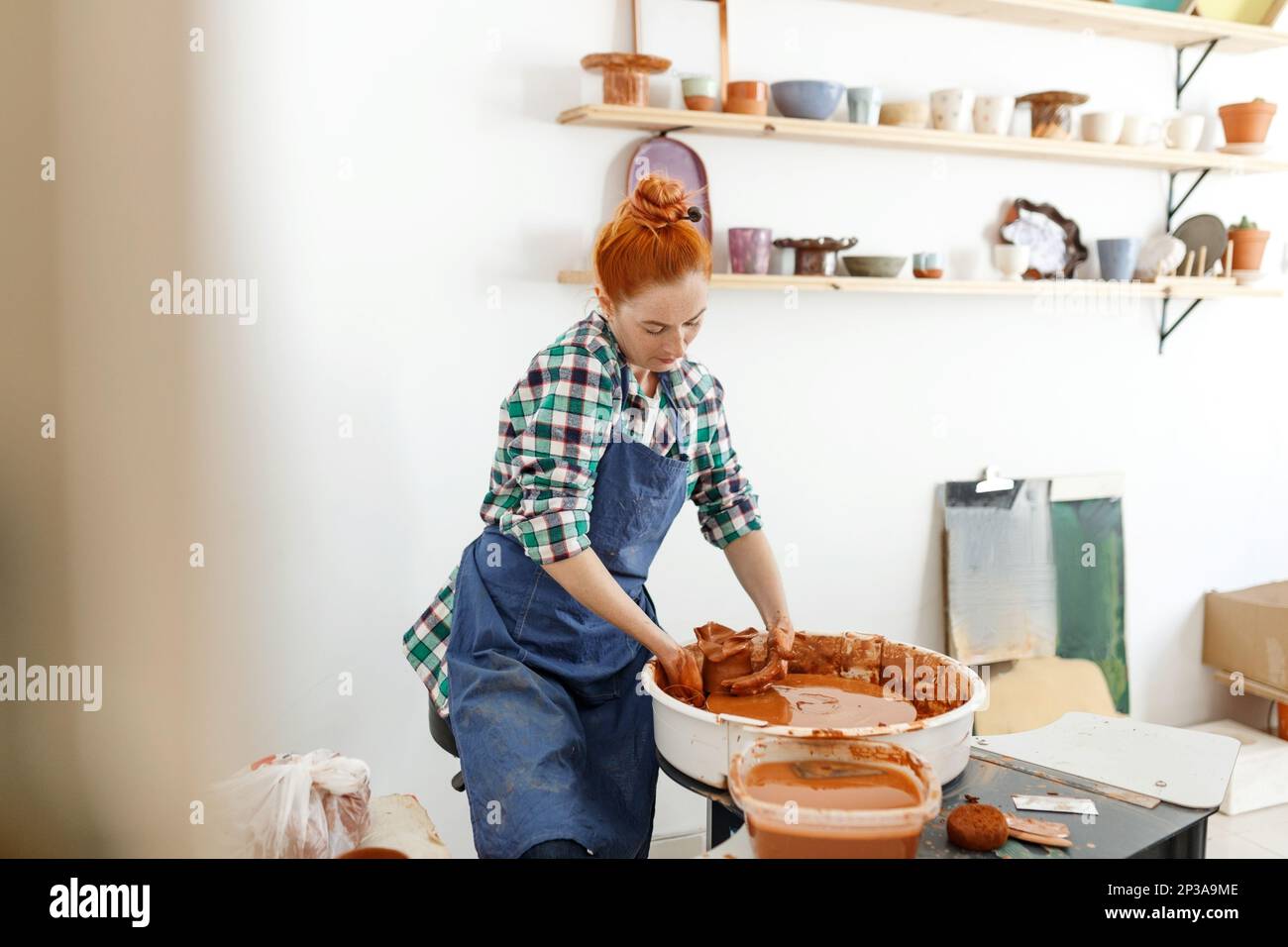 Fröhliche Bildhauerin, während sie Tontopf auf Töpferrad macht. Idee von Kleinunternehmen und Unternehmertum. Hobby, Unterhaltung und Stockfoto