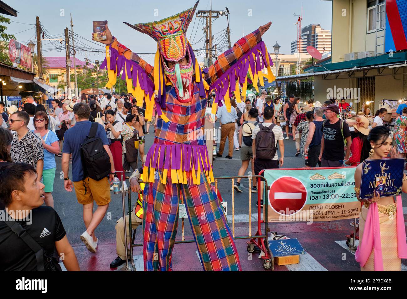 Ein bunt gekleideter Mann auf Pfählen, der während des wöchentlichen Sunday Walking Street Market für den Freizeitpark Siam Niramit in Phuket Town, Thailand wirbt Stockfoto