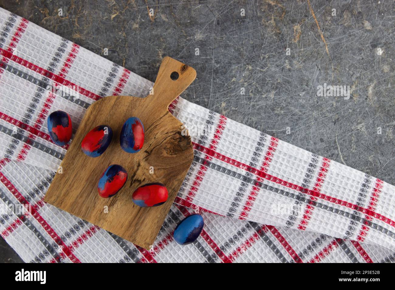 Mit einem Pinsel bemalte Eier in roten und blauen Farben liegen auf einem kleinen Holzbrett, auf einem Waffeltuch auf einem alten dunklen Marmor. Draufsicht, viel Platz Stockfoto