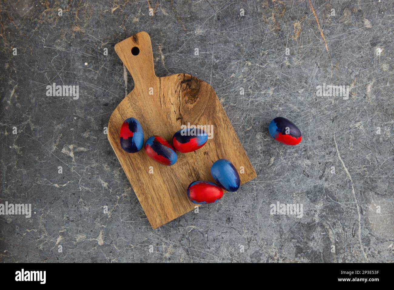 Blau-rot gefärbte Eier liegen auf einem Holzbrett auf einem alten dunklen Steintisch. Viel Platz Stockfoto