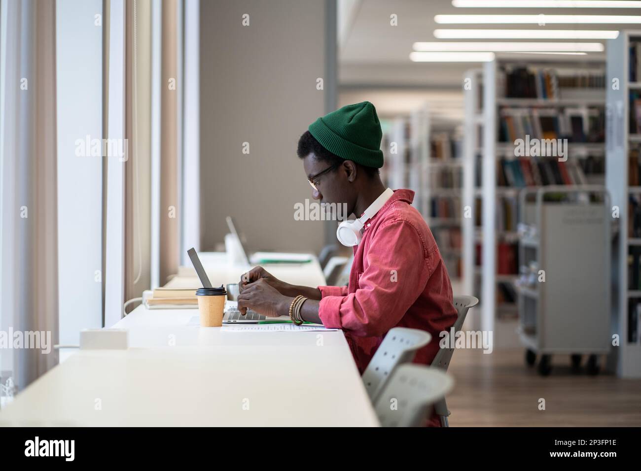 Fokussierter afroamerikanischer Student, der am Schreibtisch mit einem Laptop sitzt und eine Online-Bibliotheksdatenbank verwendet Stockfoto
