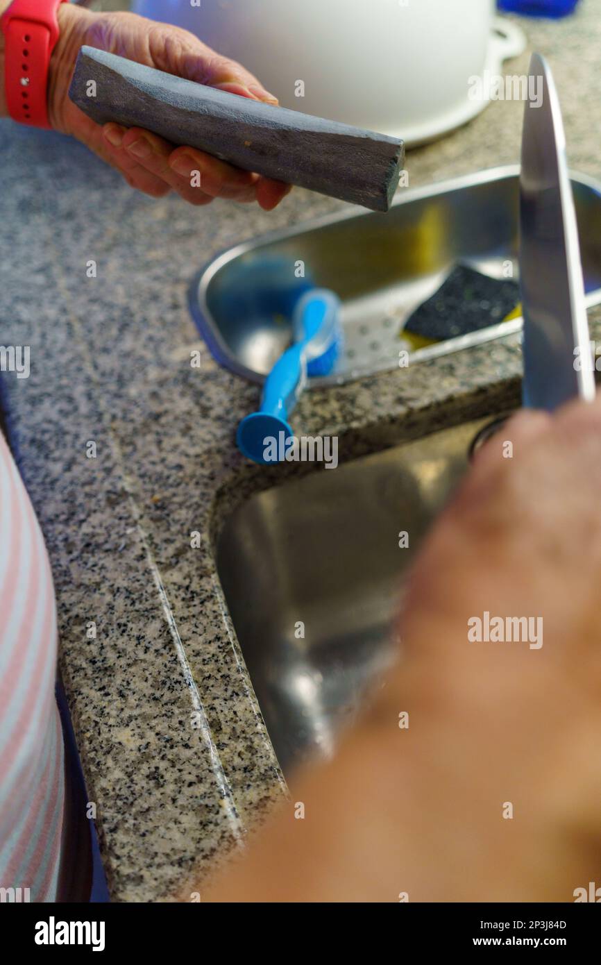 Eine Frau, die in der Küche ein Messer über dem Waschbecken schärft Stockfoto