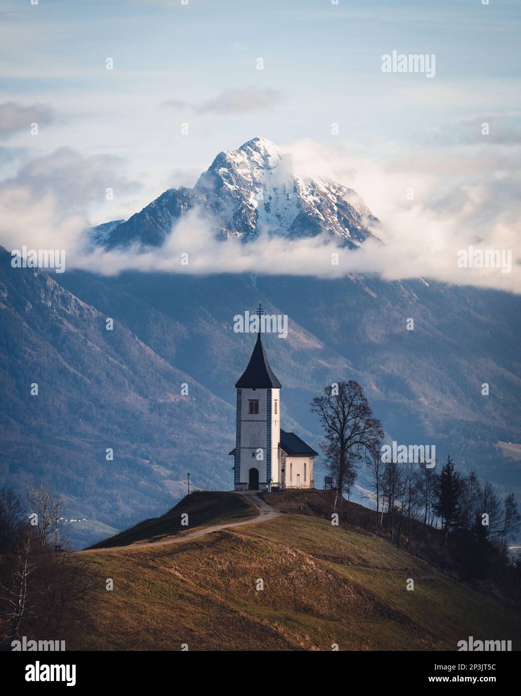 2023 01 01: Kirche auf einem Hügel in Jamnik, eingerahmt von einem Berg aus den Julischen Alpen Stockfoto
