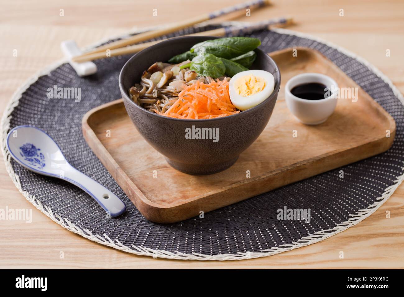 Shiitake-Pilze und Soba-Nudelsuppe mit Karotten, Spinat, gekochtem Wachtelei und Sojasoße auf einem Holztablett Stockfoto