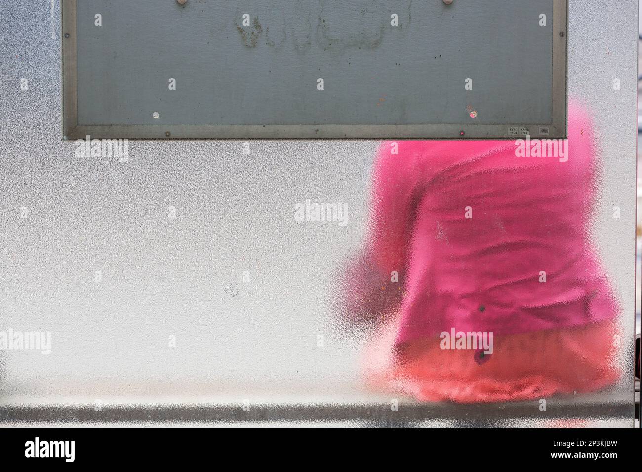 Eine Dame in einem rosa Mantel, die in einer Überdachung sitzt, mit Frostglaswänden. Brüssel. Stockfoto