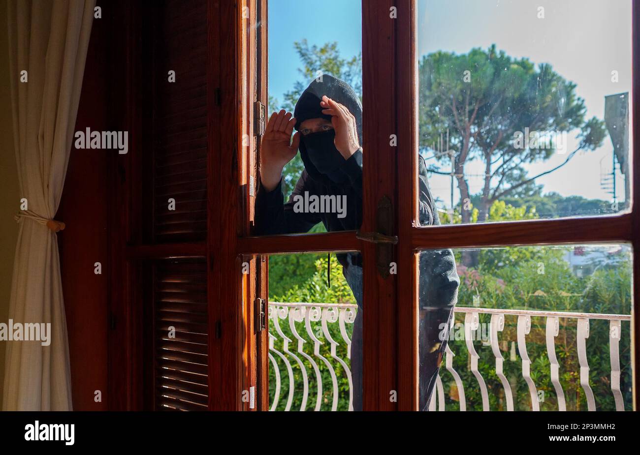 Der Dieb in der Balaklava guckt durch die Fenster. Stockfoto