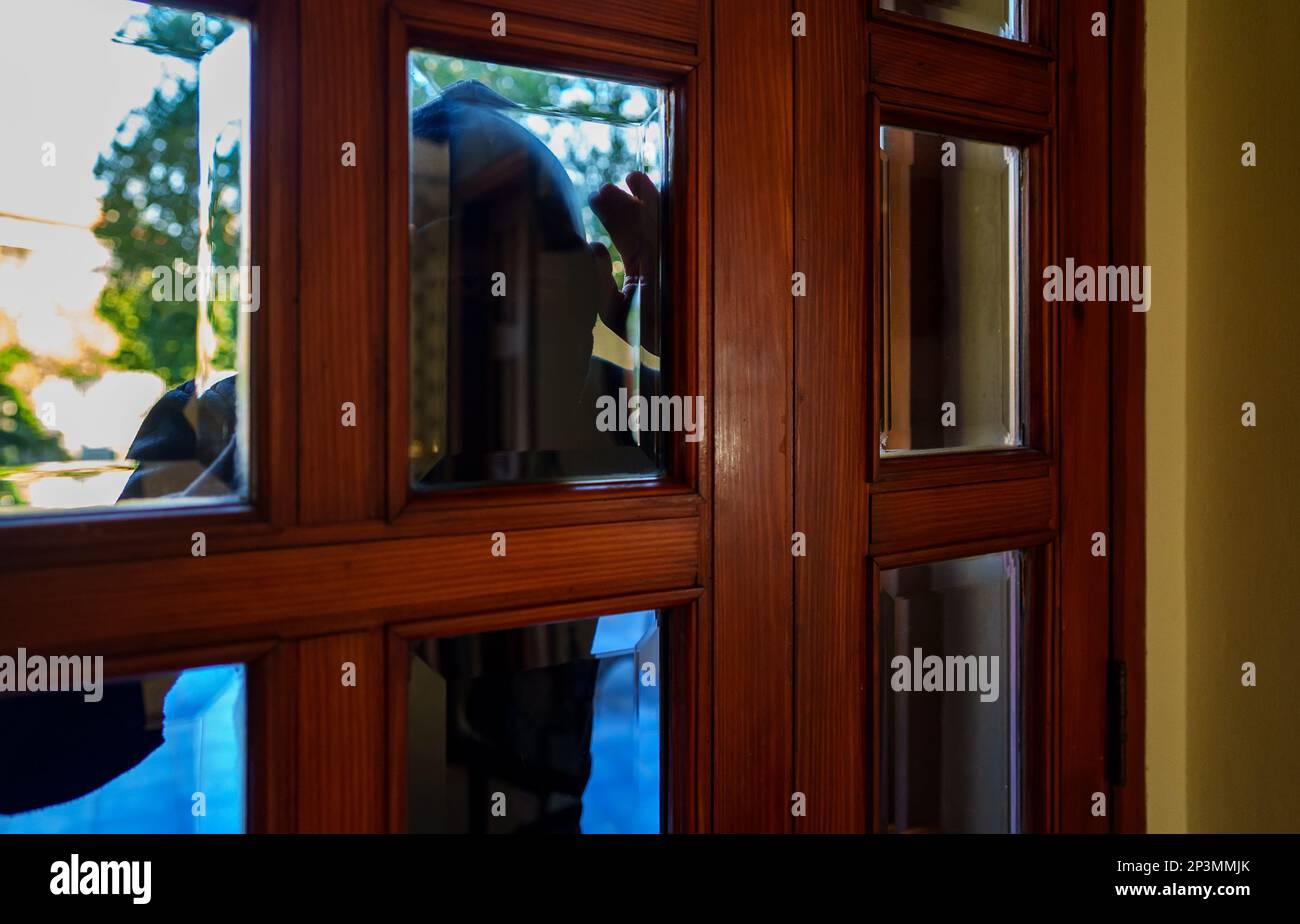 Der Dieb in der Balaklava guckt durch die Fenster. Stockfoto