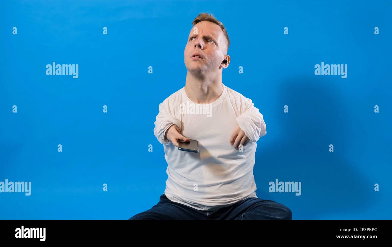 Ein Mann mit Behinderung mit angeborener Pathologie des Bewegungsapparates sieht auf einen blau isolierten Hintergrund. Stockfoto