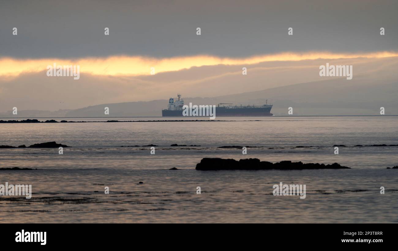 Schiff in der Ferne vor der Küste, wenn die Sonne aufgeht. Stockfoto