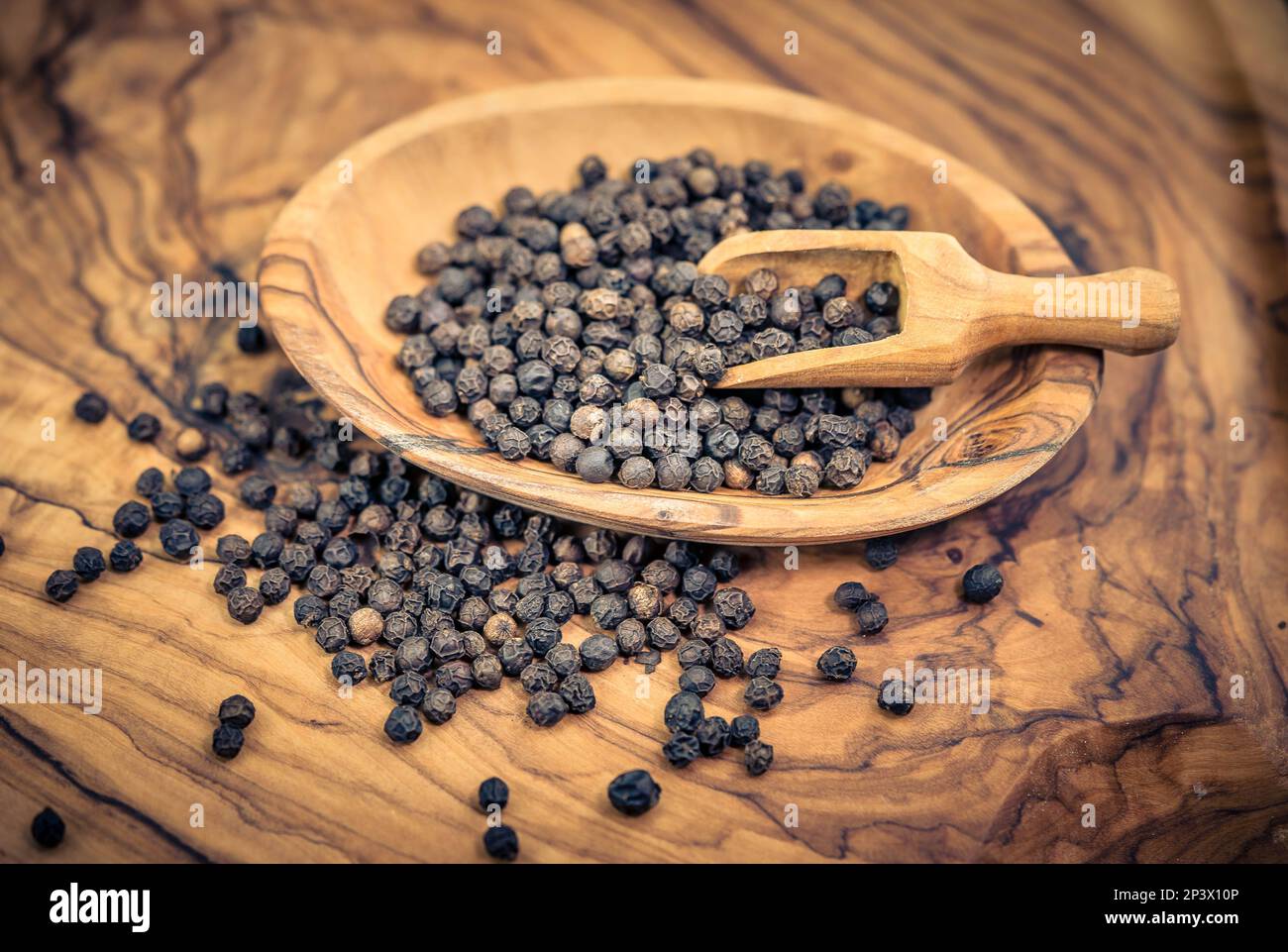 Viele schwarze Pfefferkörner auf Olivenholz Stockfoto