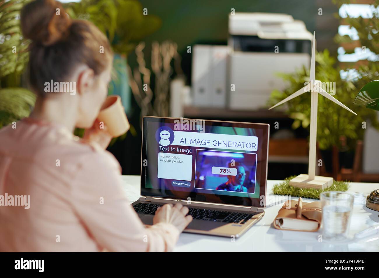 Von hinten gesehen, eine moderne Frau mit Laptop, die Text-zu-Bild-KI-Bildgenerator in einem modernen Büro verwendet. Stockfoto