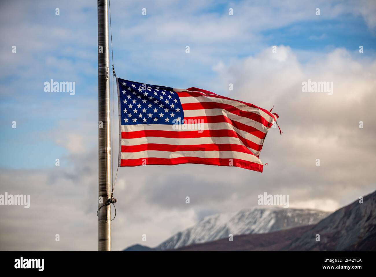 Die Flagge der Vereinigten Staaten von Amerika fliegt im Herbst mit Halbmast und blauem Himmel, Wolken und Berghintergrund im Norden. Stockfoto